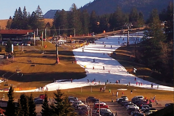 Skigebiet im Allgäu: Pistenstreifen aus Kunstschnee in ansonsten schneefreiem grünem Hang