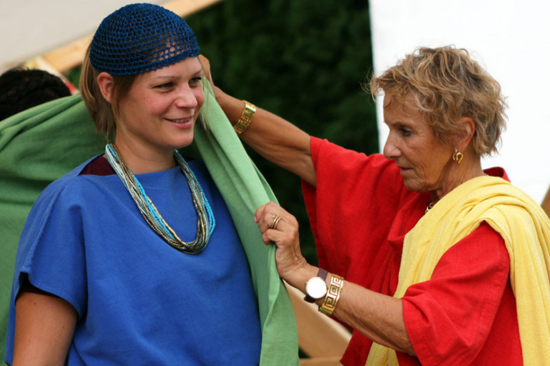 Frau hilft Jugendlicher beim Einkleiden (beide in römischem Gewand)